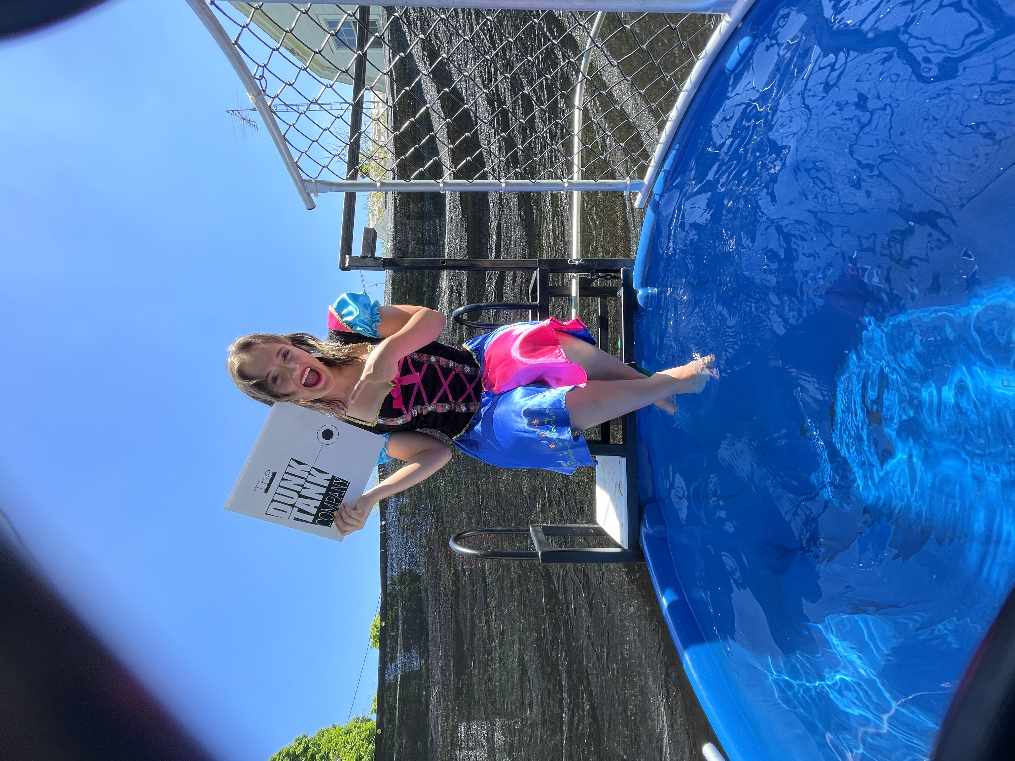Looking for a Dunk Tank Rental company? Girl sitting over a dunk tank holding a Dunk Tank Company sign